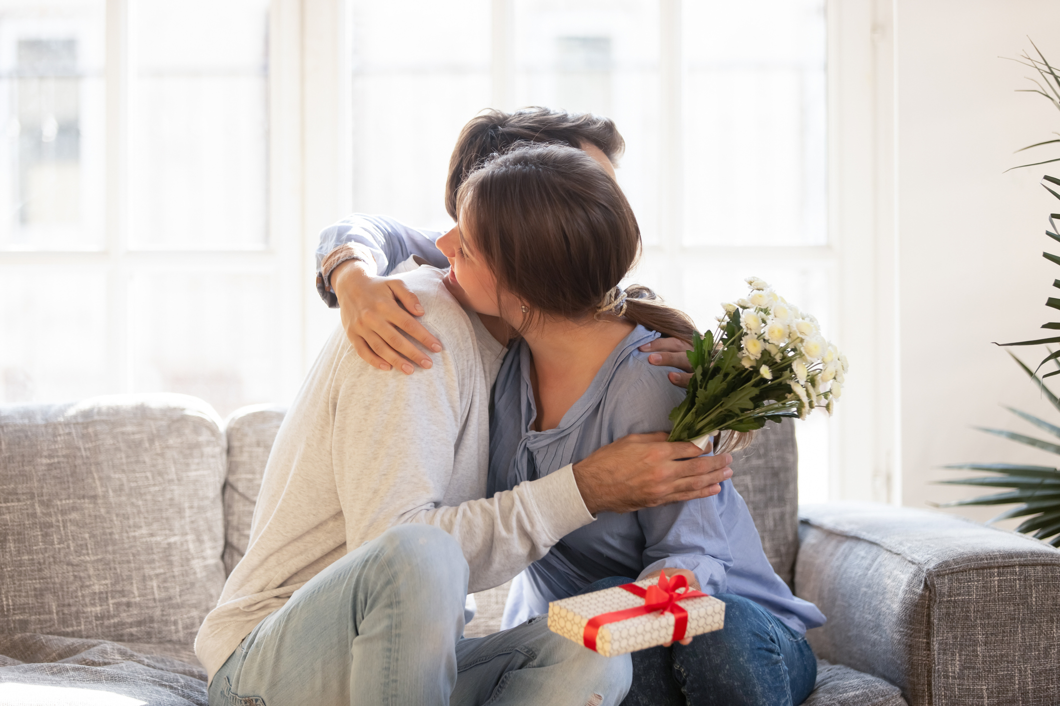 Loving wife embracing husband, thanking for romantic present, surprise, happy girlfriend receiving gift box and flowers from boyfriend, couple celebrating birthday, Valentines day, anniversary