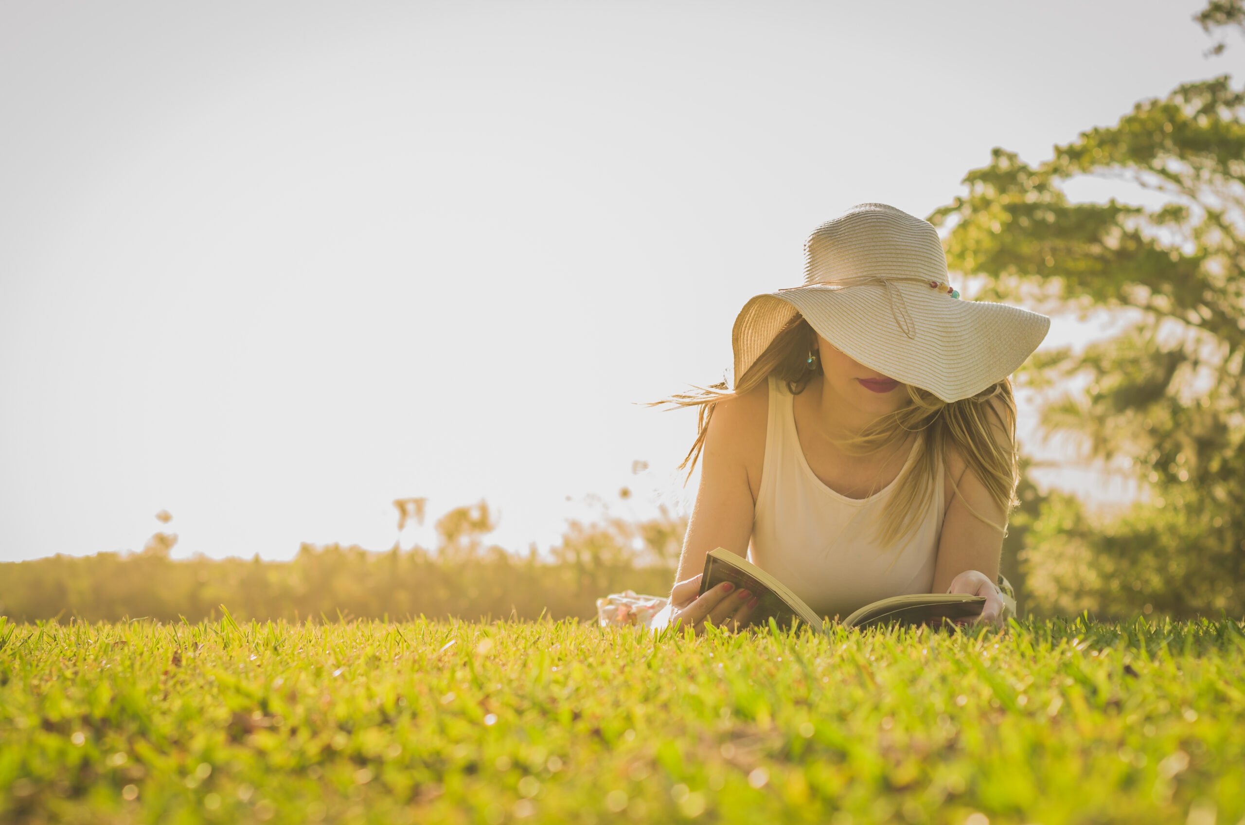 Pretty woman reading book lying on the lawn, seen from above with summer hat.